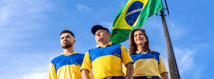 Dois homens carteiro e uma mulher carteira enfileirados olhando ao horizonte. Bandeira do Brasil hasteada atrás deles.