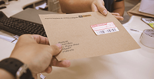 mão segurando envelope pardo com etiqueta de carta registrada
