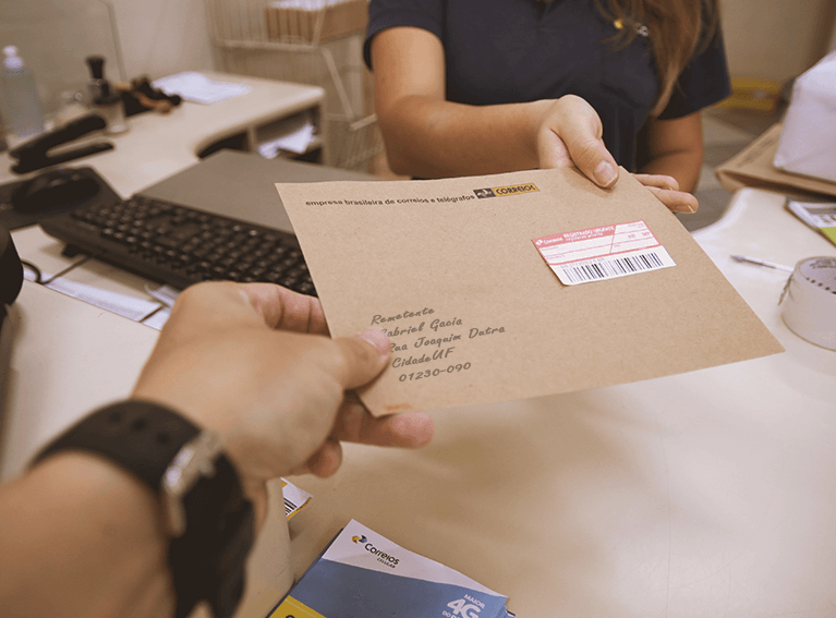Envelope pardo com etiqueta de carta registrada sendo postada em agência dos Correios